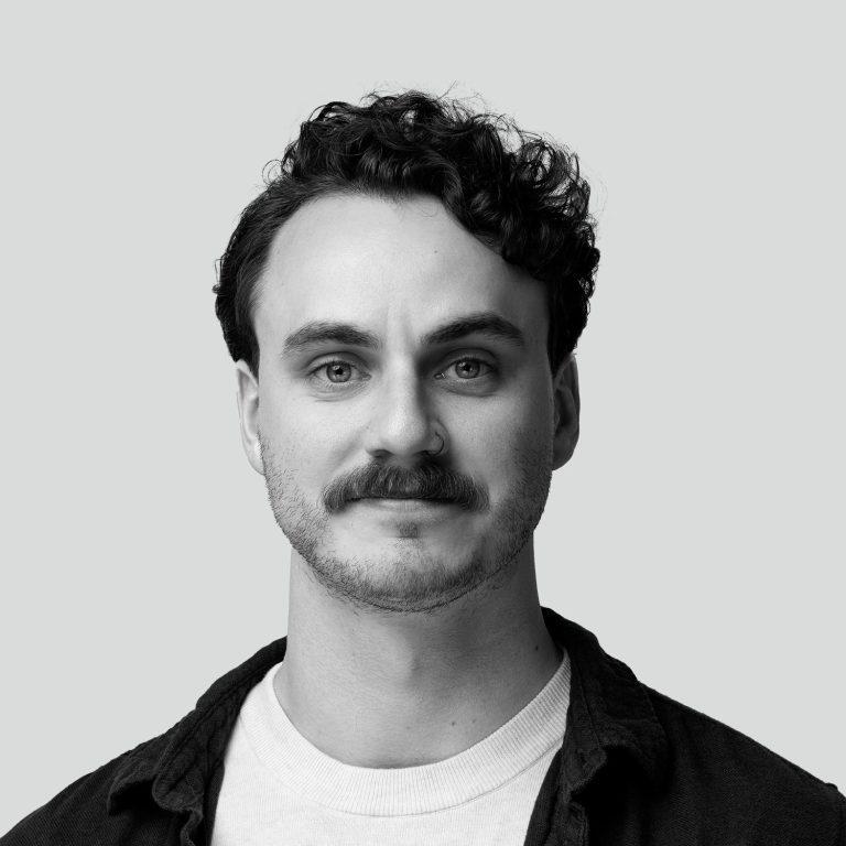 Black and white headshot of a man with curly hair and a mustache, smiling slightly.