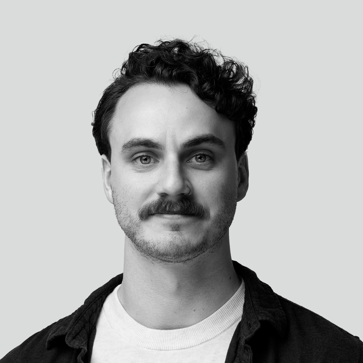 Black and white headshot of a man with curly hair and a mustache, smiling slightly.
